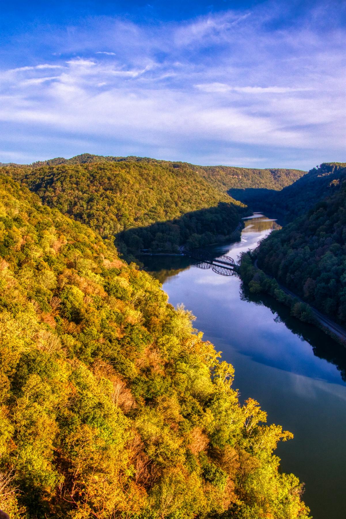 A steel truss bridge crossing a river through an autumn gorge